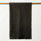 Dark brown waffle grid towel hanging on a wooden rod against a white background