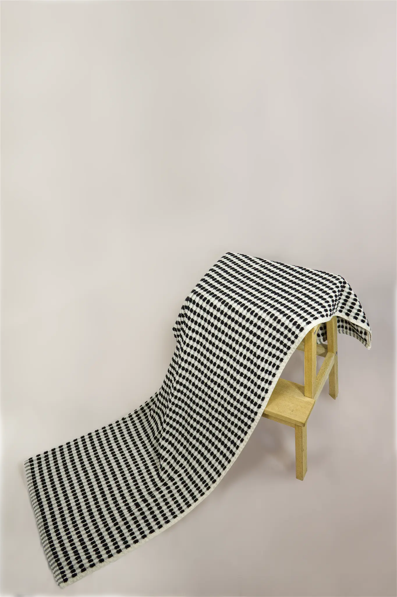 Black and white checkered bath towel draped over a wooden chair on a beige background