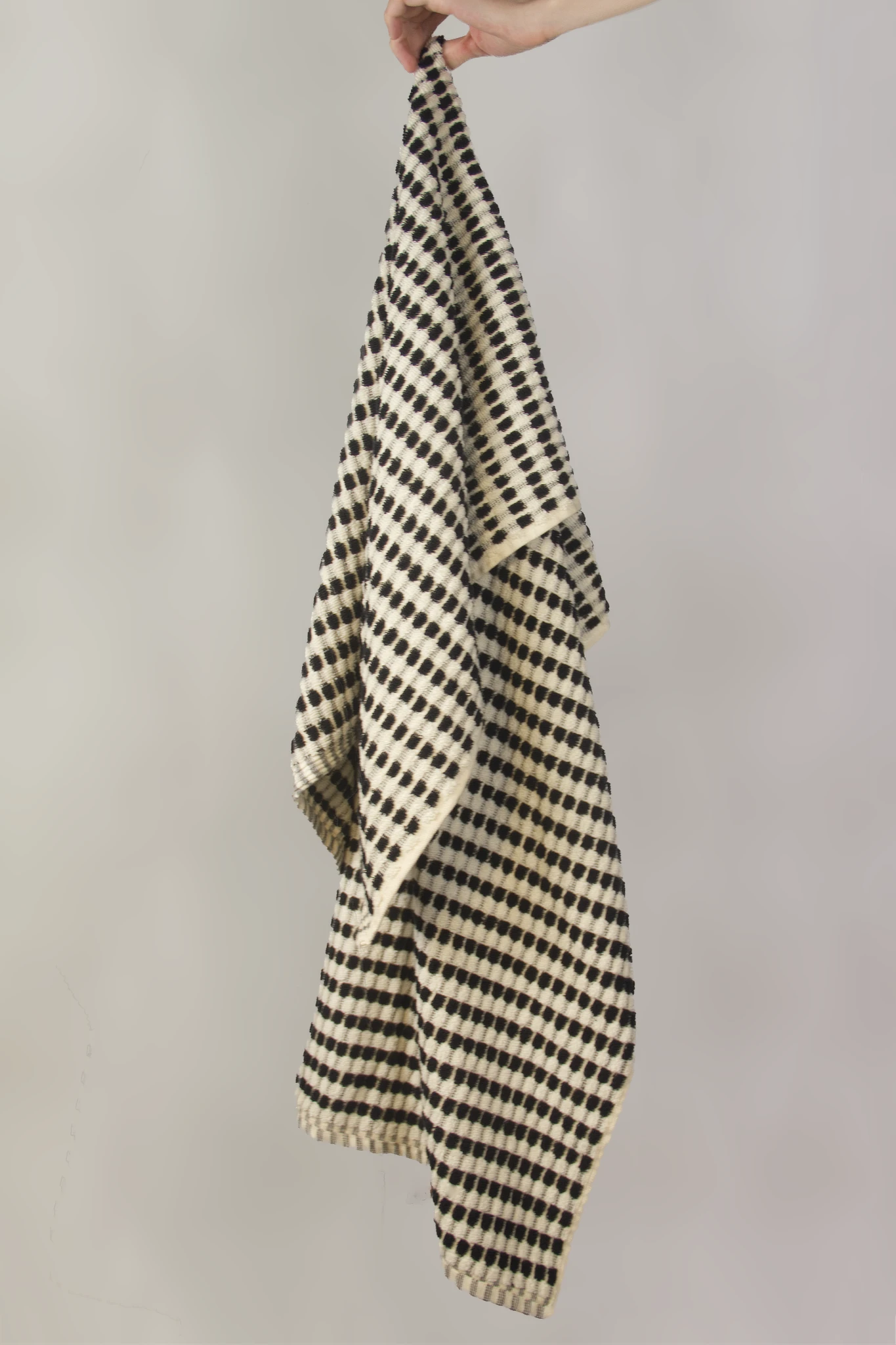 Black and white checkered towel held by a hand against a plain background