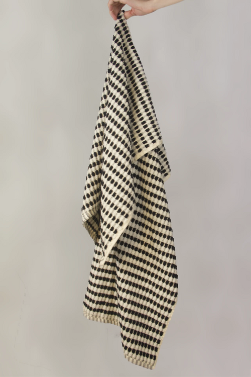 Black and white checkered towel held by a hand against a plain background